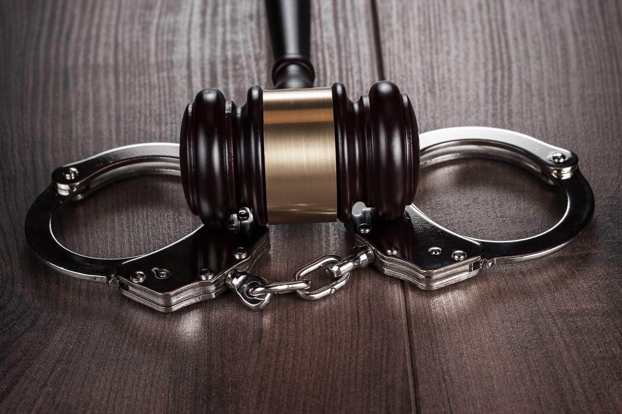 handcuffs and judge gavel on brown wooden table background
